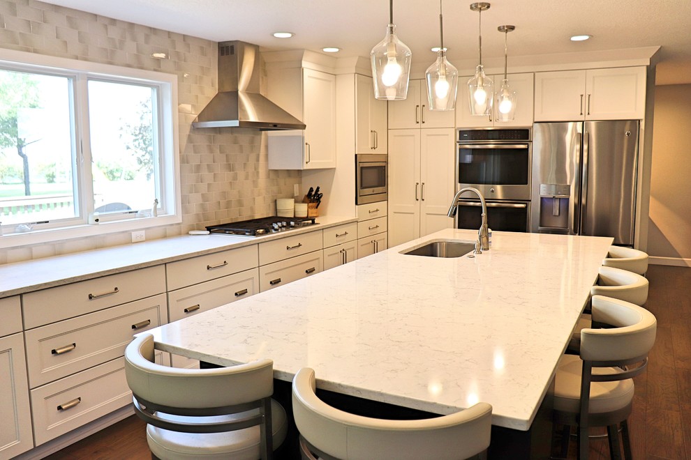 Example of a transitional l-shaped medium tone wood floor and brown floor kitchen pantry design in Cedar Rapids with an undermount sink, recessed-panel cabinets, white cabinets, quartzite countertops, gray backsplash, porcelain backsplash, stainless steel appliances, an island and white countertops