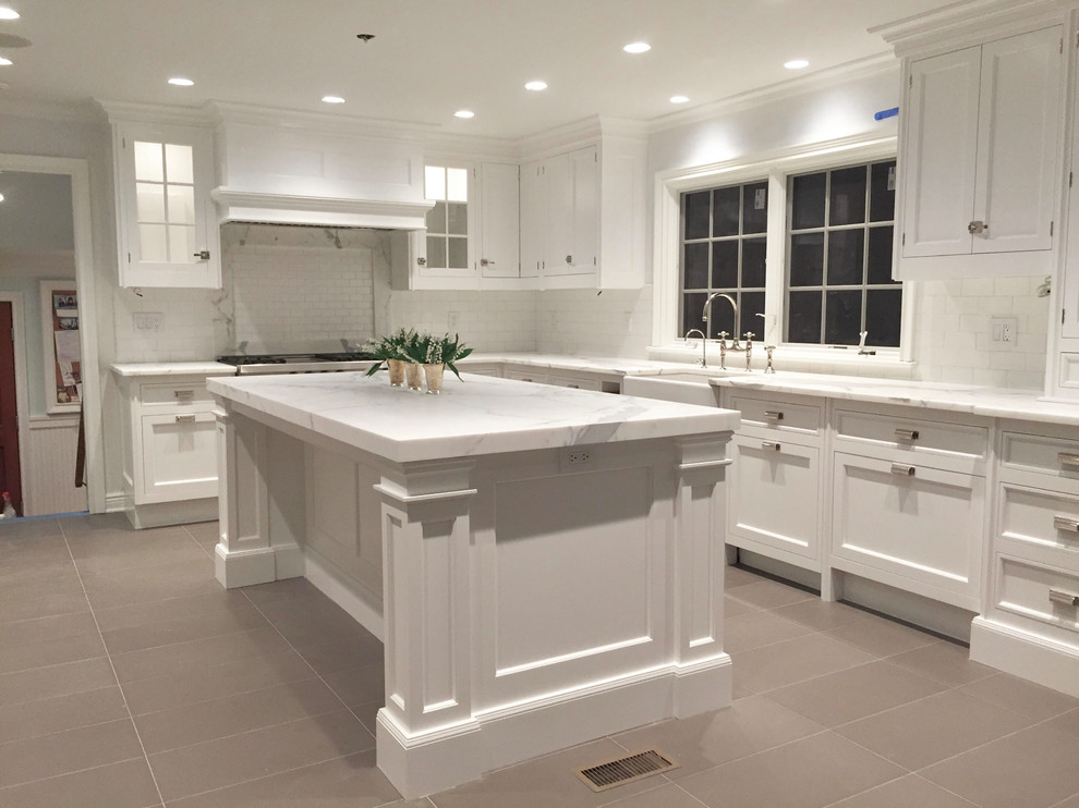 Eat-in kitchen - large transitional l-shaped beige floor eat-in kitchen idea with a farmhouse sink, shaker cabinets, white cabinets, white backsplash, stainless steel appliances and an island