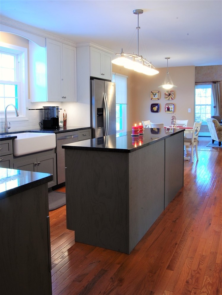 Example of a mid-sized transitional l-shaped medium tone wood floor eat-in kitchen design in Boston with a farmhouse sink, shaker cabinets, white cabinets, quartz countertops, white backsplash, subway tile backsplash, stainless steel appliances and an island
