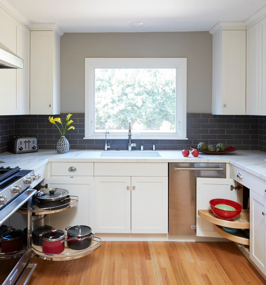 Inspiration for a mid-sized transitional u-shaped separate kitchen in San Francisco with an undermount sink, shaker cabinets, white cabinets, tile benchtops, grey splashback, stone tile splashback, stainless steel appliances, light hardwood floors and no island.
