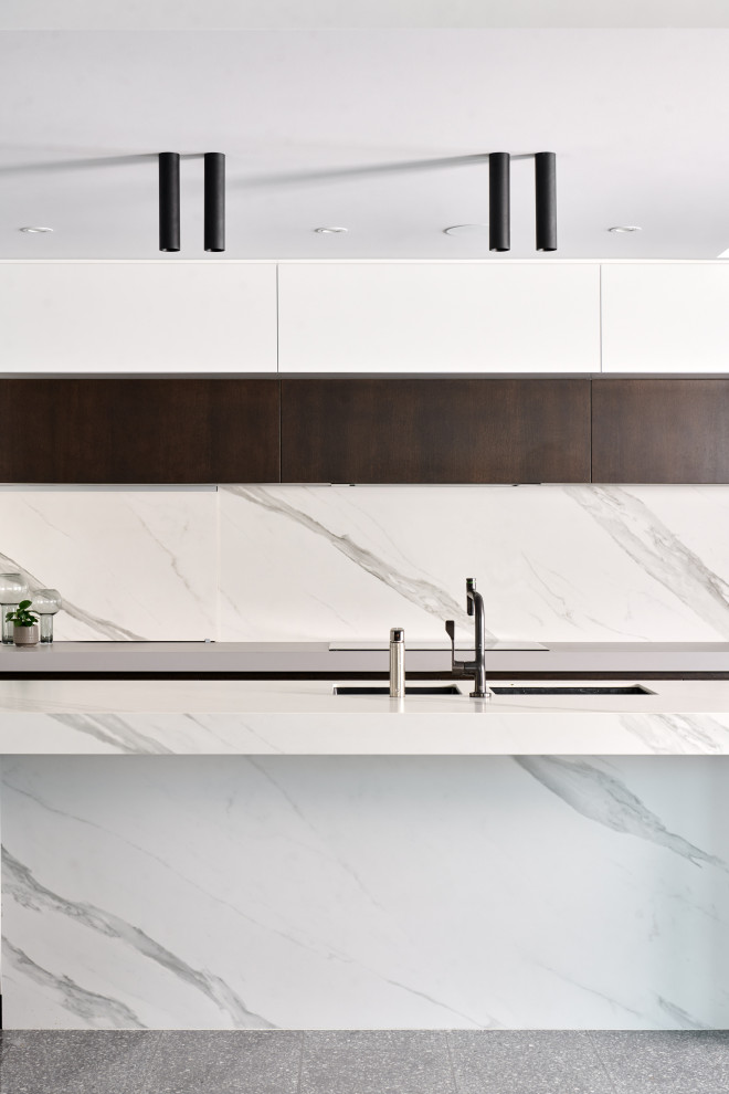 Photo of an expansive contemporary l-shaped eat-in kitchen in Perth with an undermount sink, flat-panel cabinets, white cabinets, quartz benchtops, white splashback, porcelain splashback, black appliances, concrete floors, with island, grey floor and white benchtop.