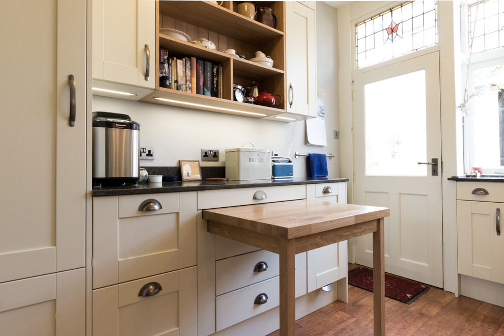 Photo of a mid-sized traditional u-shaped separate kitchen in Other with a farmhouse sink, shaker cabinets, white cabinets, recycled glass benchtops, white splashback, glass sheet splashback, white appliances, medium hardwood floors and no island.