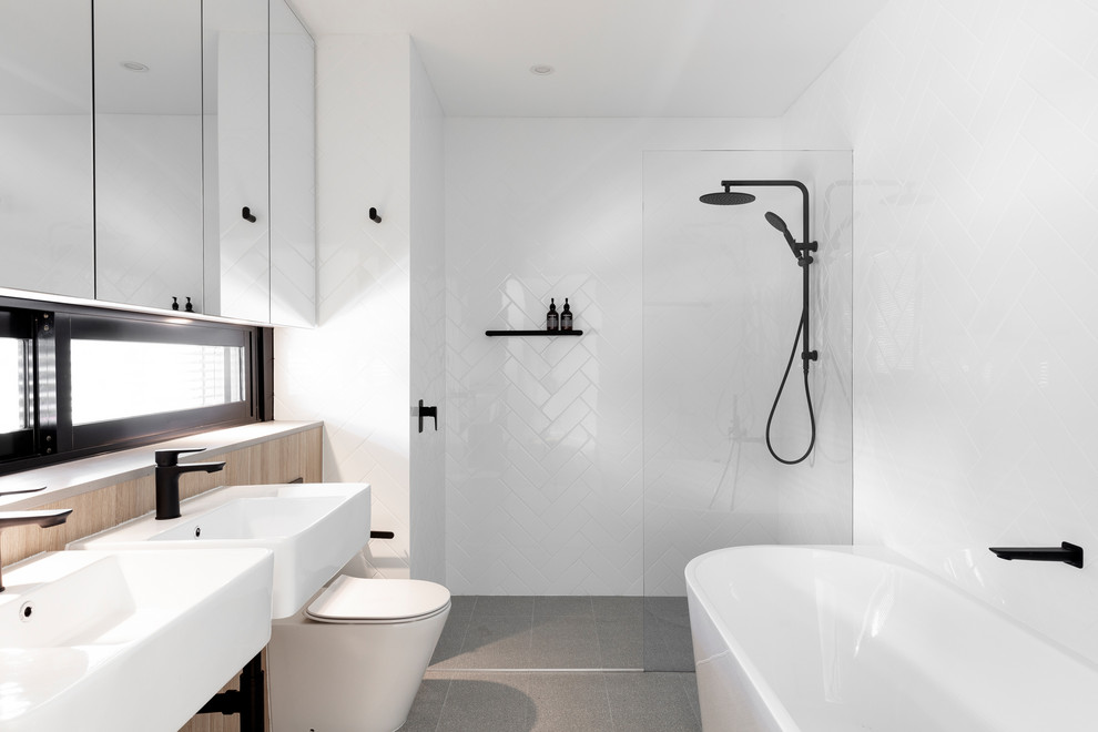 This is an example of a contemporary master bathroom in Sydney with white tile, white walls, a wall-mount sink, grey floor, an open shower, a freestanding tub, an alcove shower and a one-piece toilet.