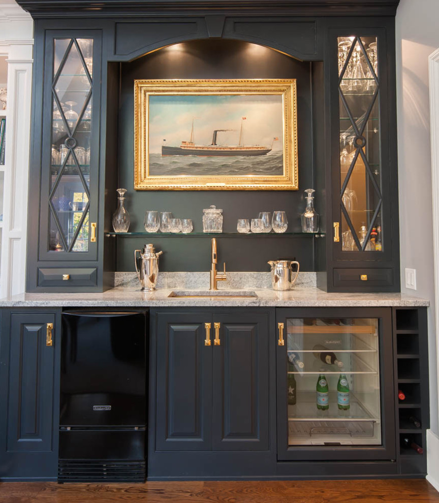 Small traditional single-wall wet bar in New York with an undermount sink, raised-panel cabinets, blue cabinets, granite benchtops, medium hardwood floors and brown floor.