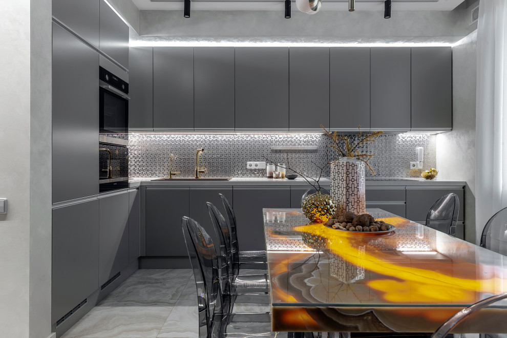 This is an example of a contemporary l-shaped eat-in kitchen in Moscow with a drop-in sink, flat-panel cabinets, grey cabinets, metallic splashback, mosaic tile splashback, black appliances, grey floor and grey benchtop.