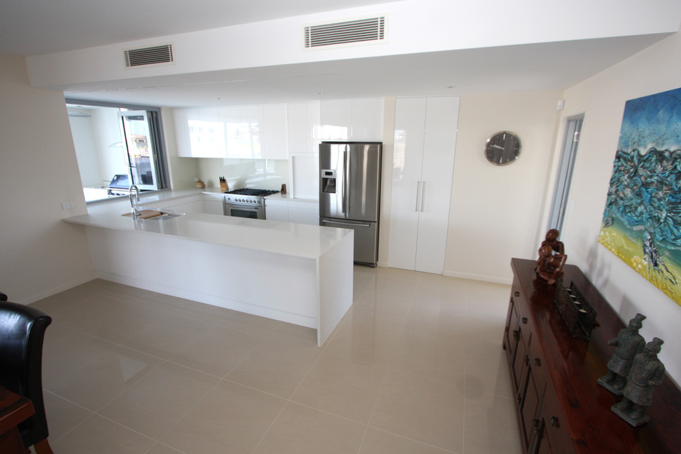 Mid-sized modern u-shaped eat-in kitchen in Sunshine Coast with a drop-in sink, flat-panel cabinets, white cabinets, quartz benchtops, white splashback, glass sheet splashback, stainless steel appliances, porcelain floors and with island.