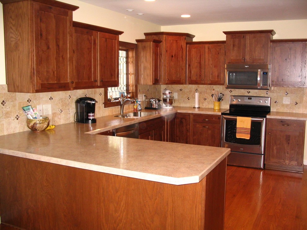 Eat-in kitchen - u-shaped medium tone wood floor eat-in kitchen idea with a drop-in sink, recessed-panel cabinets, medium tone wood cabinets, solid surface countertops, beige backsplash, ceramic backsplash, stainless steel appliances and no island