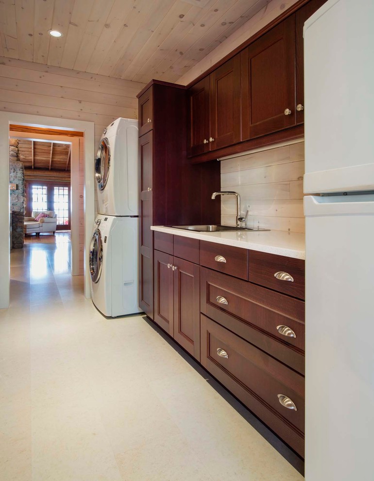 Photo of a large country utility room in Other with a drop-in sink, dark wood cabinets, white walls, a stacked washer and dryer and white benchtop.
