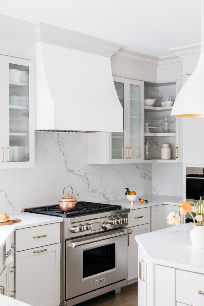 Modern inredning av ett stort vit vitt kök, med en nedsänkt diskho, luckor med infälld panel, vita skåp, bänkskiva i kvartsit, flerfärgad stänkskydd, stänkskydd i marmor, rostfria vitvaror, mellanmörkt trägolv, en köksö och brunt golv