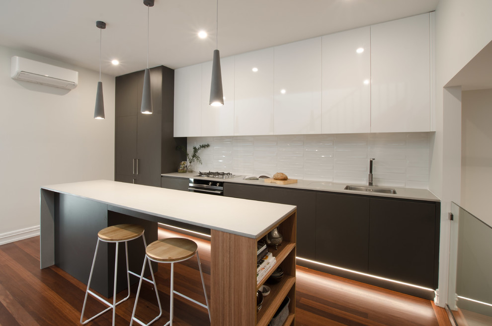Inspiration for a small modern galley open plan kitchen in Sydney with an integrated sink, flat-panel cabinets, grey cabinets, quartz benchtops, white splashback, ceramic splashback, black appliances, dark hardwood floors, with island and brown floor.