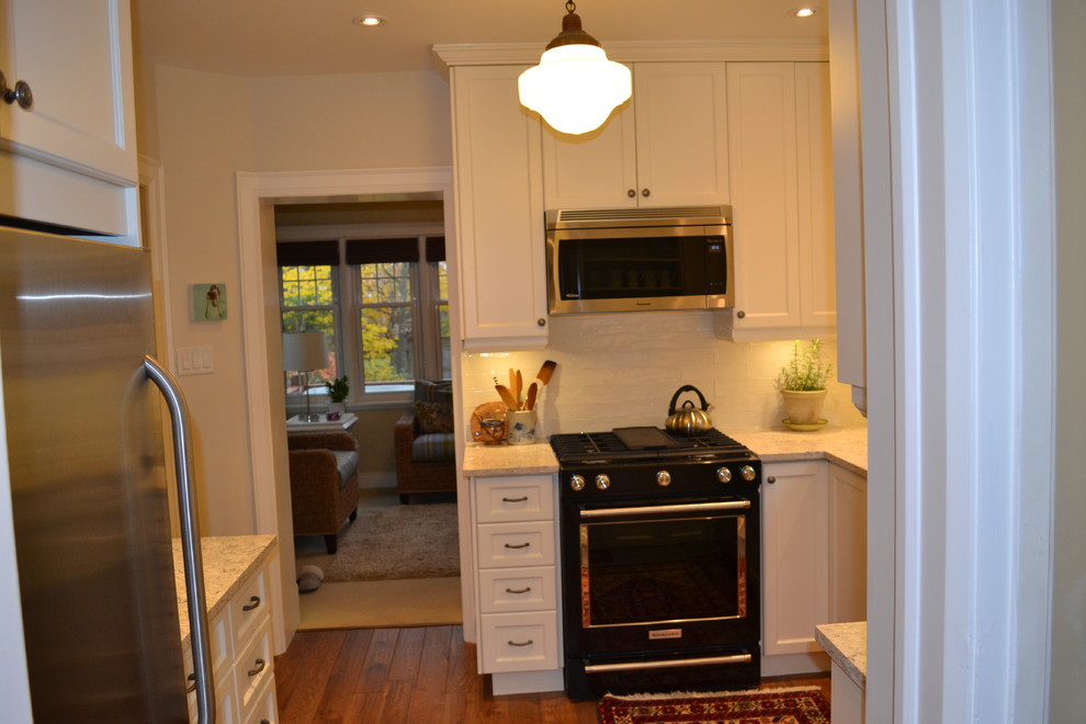 Small transitional galley medium tone wood floor enclosed kitchen photo in Toronto with an undermount sink, white backsplash, porcelain backsplash, stainless steel appliances, no island, white cabinets, recessed-panel cabinets and quartz countertops