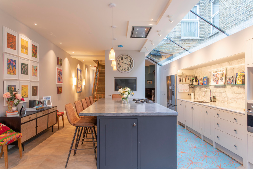 Design ideas for a contemporary galley kitchen in London with an undermount sink, flat-panel cabinets, white cabinets, grey splashback, stone slab splashback, stainless steel appliances, with island, blue floor and grey benchtop.
