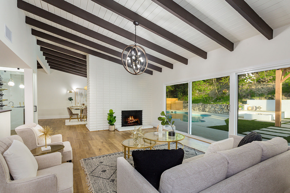 Photo of a midcentury open concept living room in Los Angeles with white walls, medium hardwood floors, a standard fireplace, a brick fireplace surround, brown floor, exposed beam, timber and vaulted.