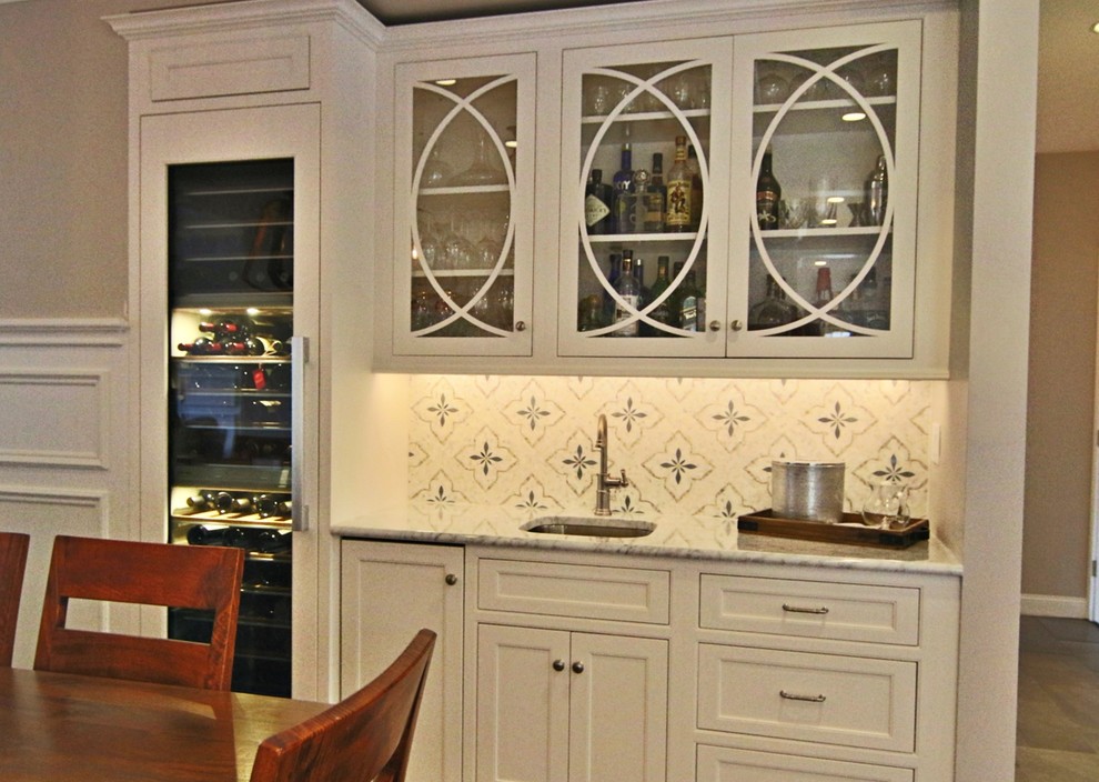 Inspiration for a large transitional l-shaped laminate floor and brown floor open concept kitchen remodel in Boston with a farmhouse sink, recessed-panel cabinets, white cabinets, marble countertops, white backsplash, marble backsplash, paneled appliances and an island