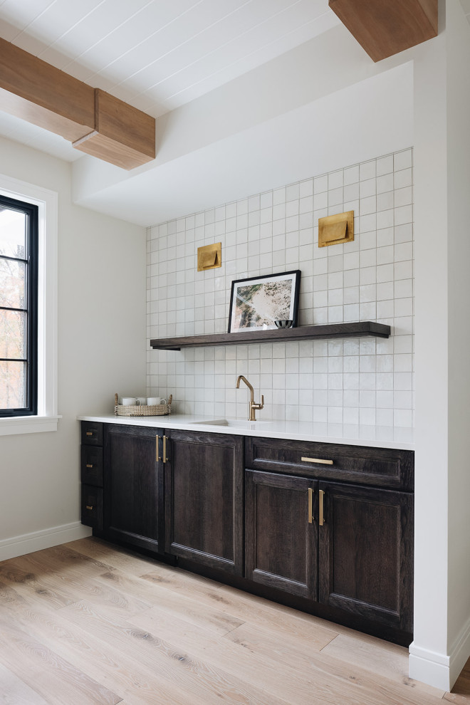 Coffee Bar - Coffee bar featuring dark wood cabinetry, white square tile backsplash, gold faucet, white countertop, gold hardware, brass sconces, and open shelving.