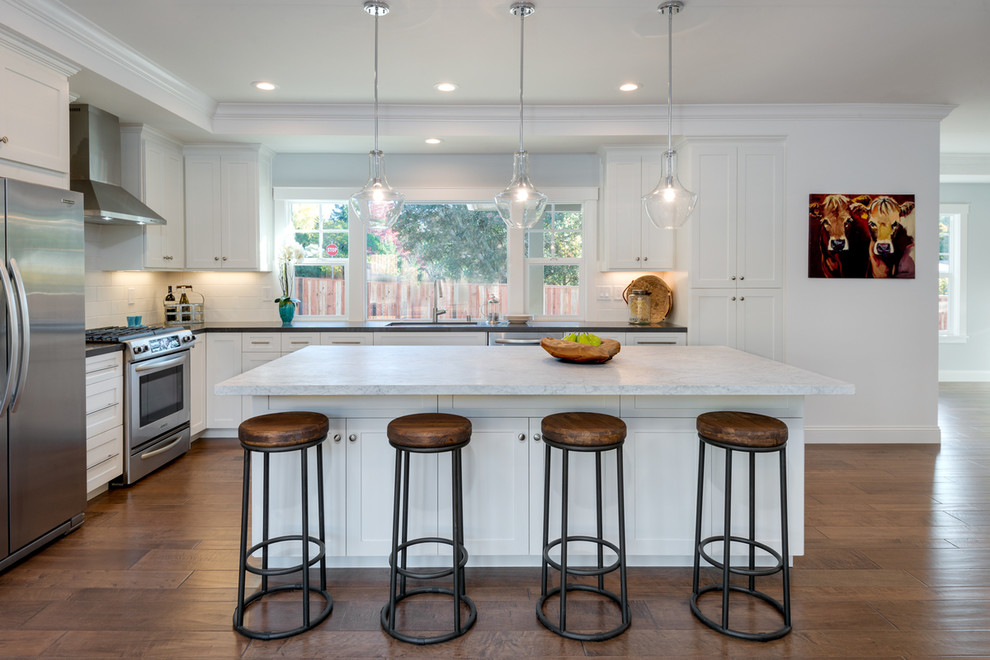 This is an example of a mid-sized country l-shaped eat-in kitchen in San Francisco with shaker cabinets, white cabinets, marble benchtops, white splashback, subway tile splashback, stainless steel appliances, medium hardwood floors, with island, an undermount sink and beige floor.