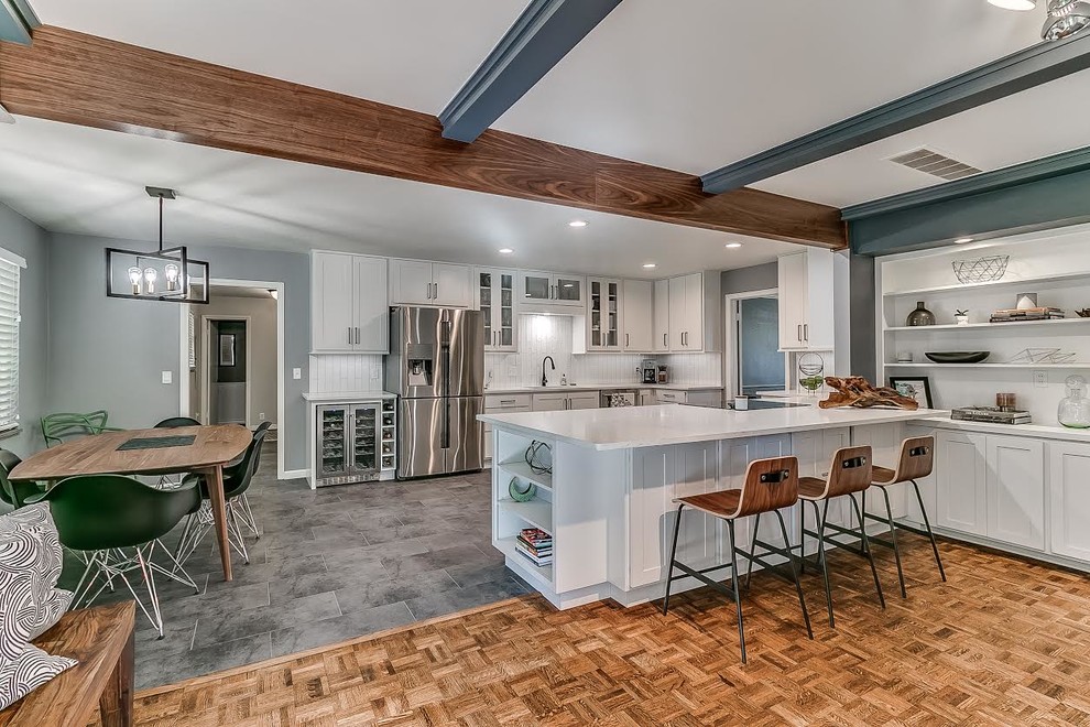 Photo of a large contemporary u-shaped eat-in kitchen in Oklahoma City with grey floor, stainless steel appliances, white splashback, glass tile splashback, white cabinets, solid surface benchtops, an undermount sink, shaker cabinets, porcelain floors, a peninsula and white benchtop.