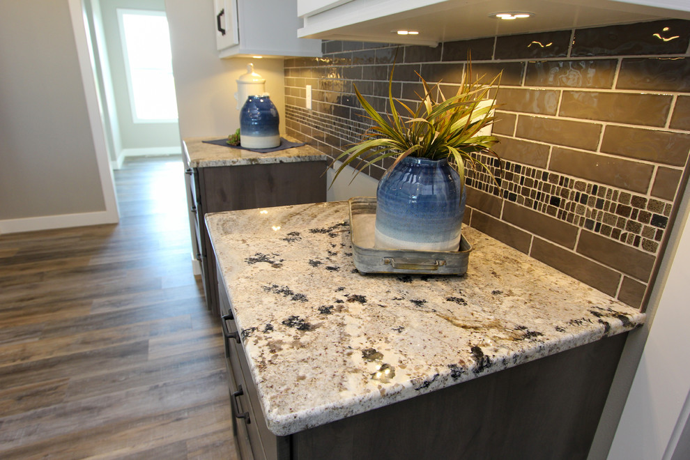 Example of a mid-sized transitional l-shaped laminate floor and brown floor eat-in kitchen design in Minneapolis with an undermount sink, shaker cabinets, white cabinets, granite countertops, gray backsplash, ceramic backsplash, an island and multicolored countertops