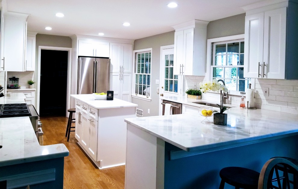 Example of a large transitional u-shaped medium tone wood floor and brown floor enclosed kitchen design in Miami with shaker cabinets, white cabinets, quartz countertops, white backsplash, subway tile backsplash, stainless steel appliances, an island, white countertops and an undermount sink