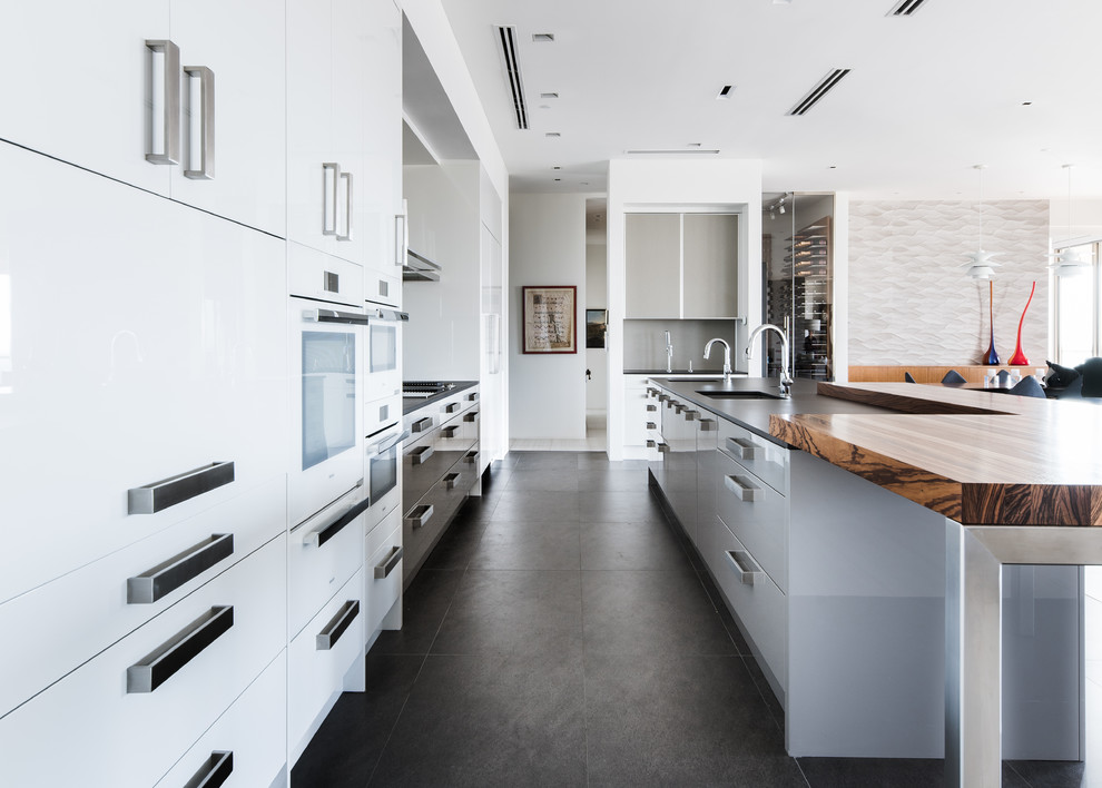 Large contemporary galley eat-in kitchen in Dallas with an undermount sink, flat-panel cabinets, white cabinets, quartz benchtops, grey splashback, porcelain splashback, white appliances, porcelain floors, with island and grey floor.