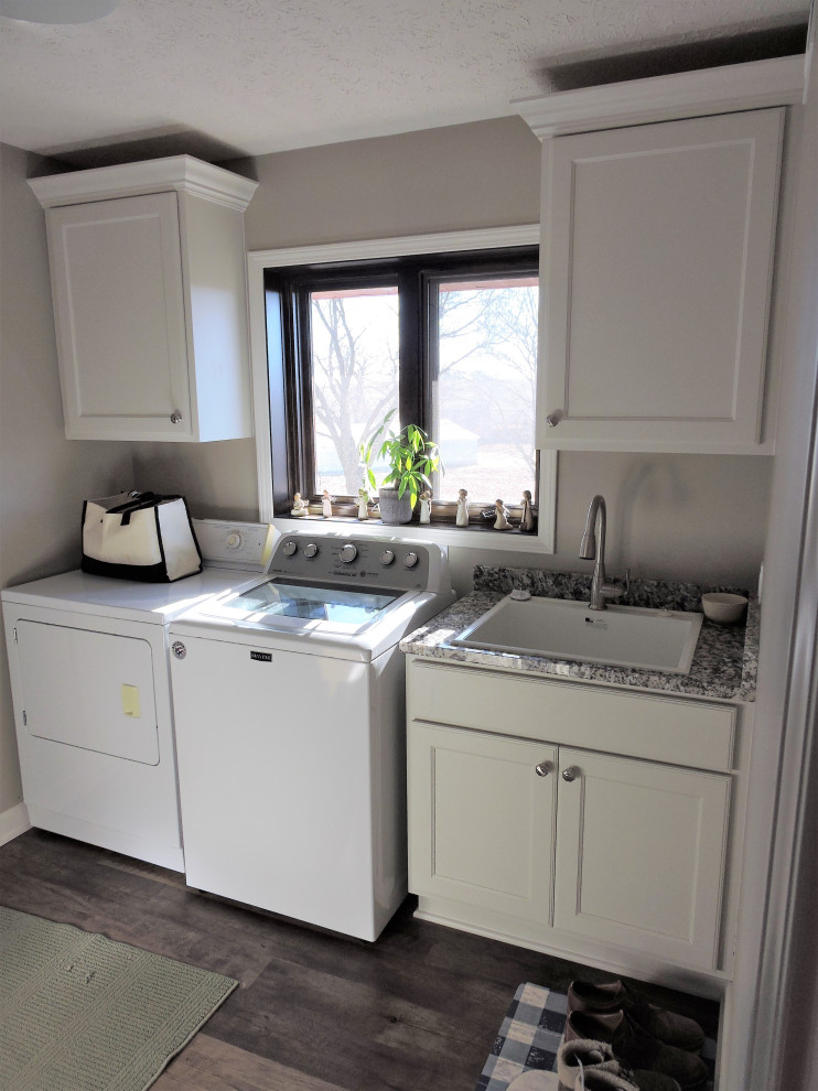 Mid-sized traditional single-wall dedicated laundry room in Omaha with an utility sink, recessed-panel cabinets, white cabinets, granite benchtops, brown splashback, granite splashback, grey walls, vinyl floors, a side-by-side washer and dryer, brown floor and brown benchtop.