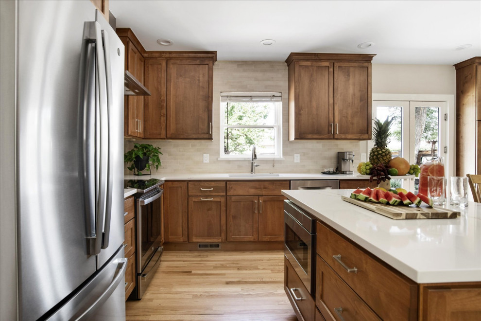 Eat-in kitchen - small transitional l-shaped light wood floor and brown floor eat-in kitchen idea in Denver with an undermount sink, shaker cabinets, medium tone wood cabinets, beige backsplash, stainless steel appliances, an island and white countertops