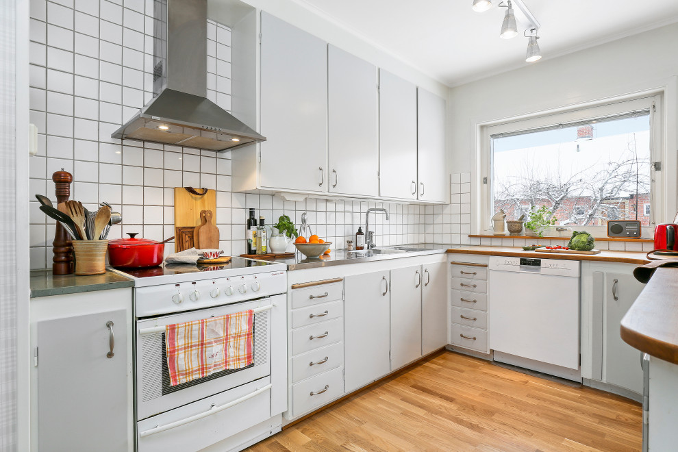 Photo of a mid-sized midcentury u-shaped separate kitchen in Stockholm with a double-bowl sink, flat-panel cabinets, grey cabinets, stainless steel benchtops, white splashback, stainless steel appliances, medium hardwood floors, brown floor and grey benchtop.