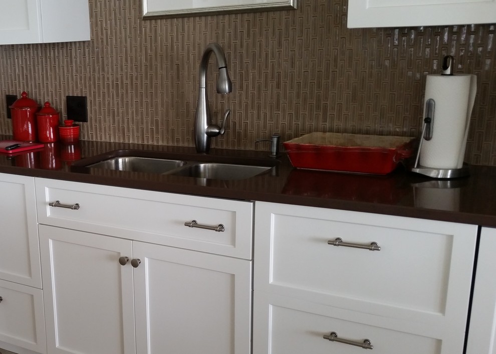 Transitional ceramic tile eat-in kitchen photo in Boston with a double-bowl sink, recessed-panel cabinets, white cabinets, quartz countertops, brown backsplash, glass tile backsplash, stainless steel appliances and an island