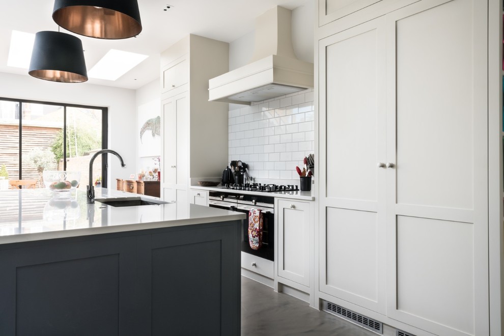 Inspiration for a large transitional galley open plan kitchen in London with a drop-in sink, shaker cabinets, grey cabinets, solid surface benchtops, stainless steel appliances, concrete floors, with island, grey floor and white benchtop.