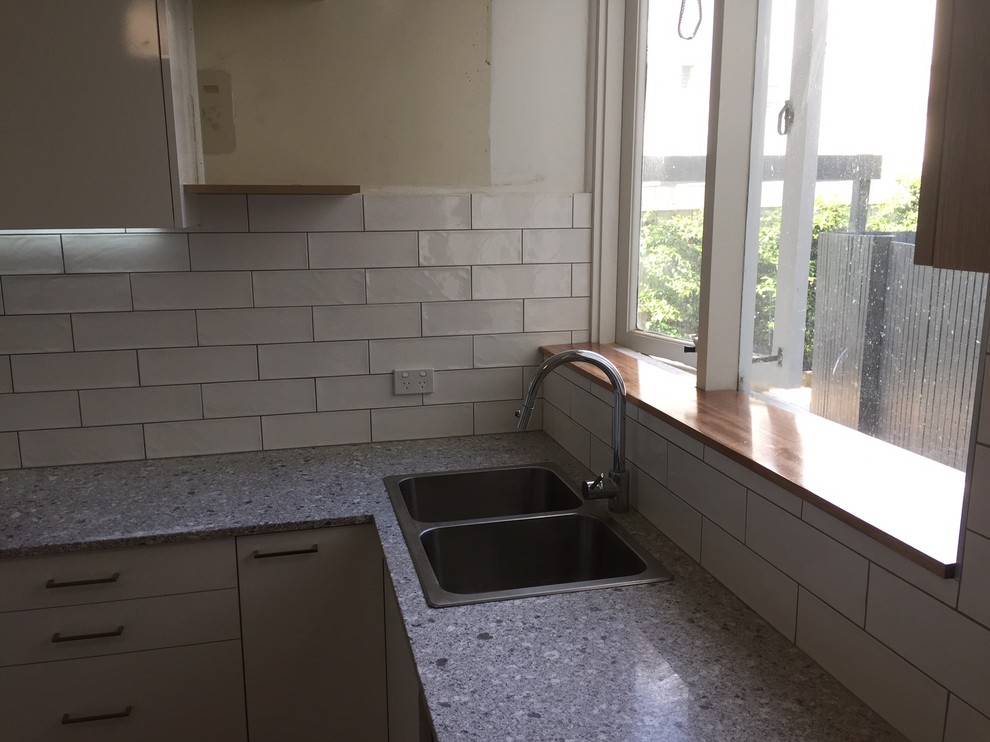Small contemporary u-shaped separate kitchen in Melbourne with a double-bowl sink, flat-panel cabinets, white cabinets, granite benchtops, white splashback, stainless steel appliances, medium hardwood floors, ceramic splashback and grey benchtop.