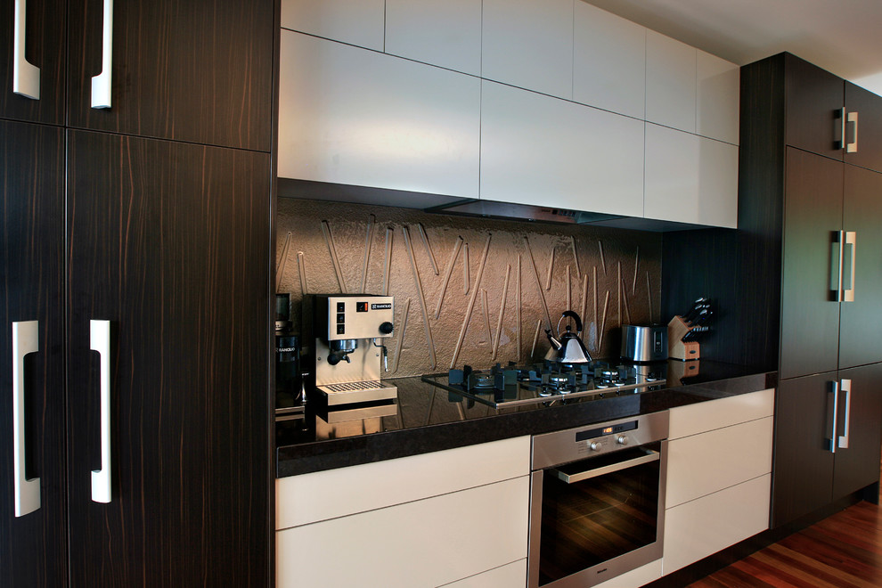 This is an example of a mid-sized contemporary galley eat-in kitchen in Brisbane with a double-bowl sink, flat-panel cabinets, dark wood cabinets, granite benchtops, beige splashback, glass sheet splashback, stainless steel appliances, light hardwood floors and with island.