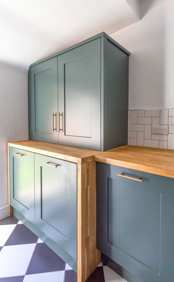Design ideas for a mid-sized transitional galley separate kitchen in Manchester with a farmhouse sink, shaker cabinets, green cabinets, wood benchtops, white splashback, subway tile splashback, stainless steel appliances, porcelain floors, a peninsula, white floor and brown benchtop.