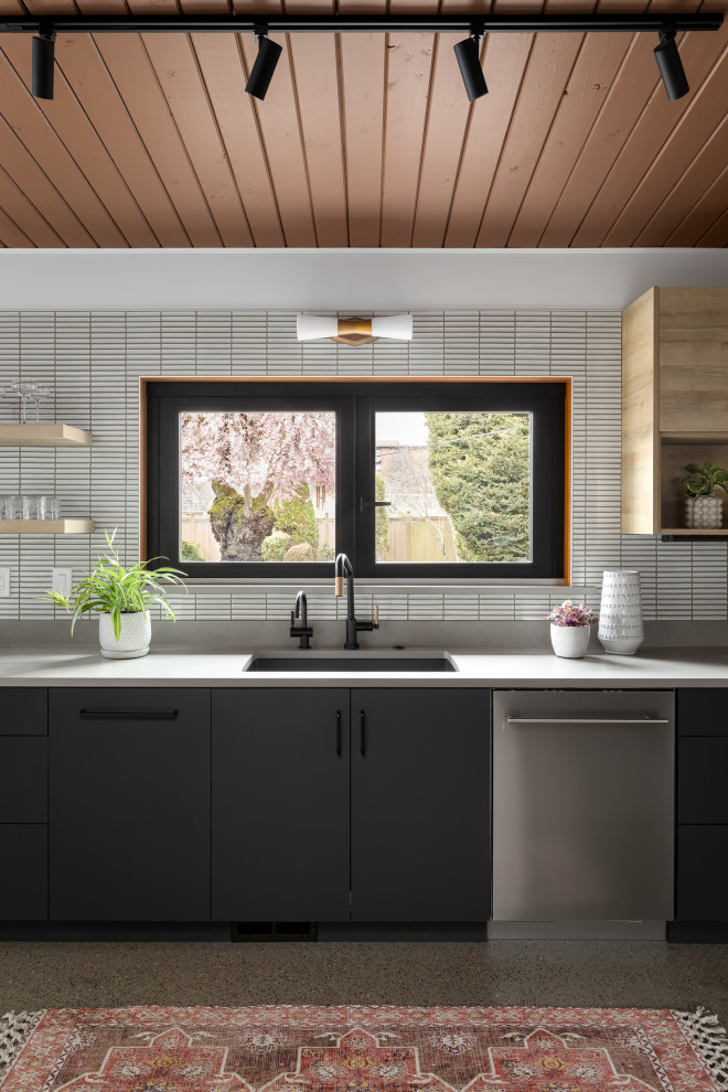Mid-sized midcentury galley eat-in kitchen in Seattle with a single-bowl sink, flat-panel cabinets, black cabinets, quartz benchtops, white splashback, mosaic tile splashback, stainless steel appliances, concrete floors, no island, grey floor, grey benchtop and wood.