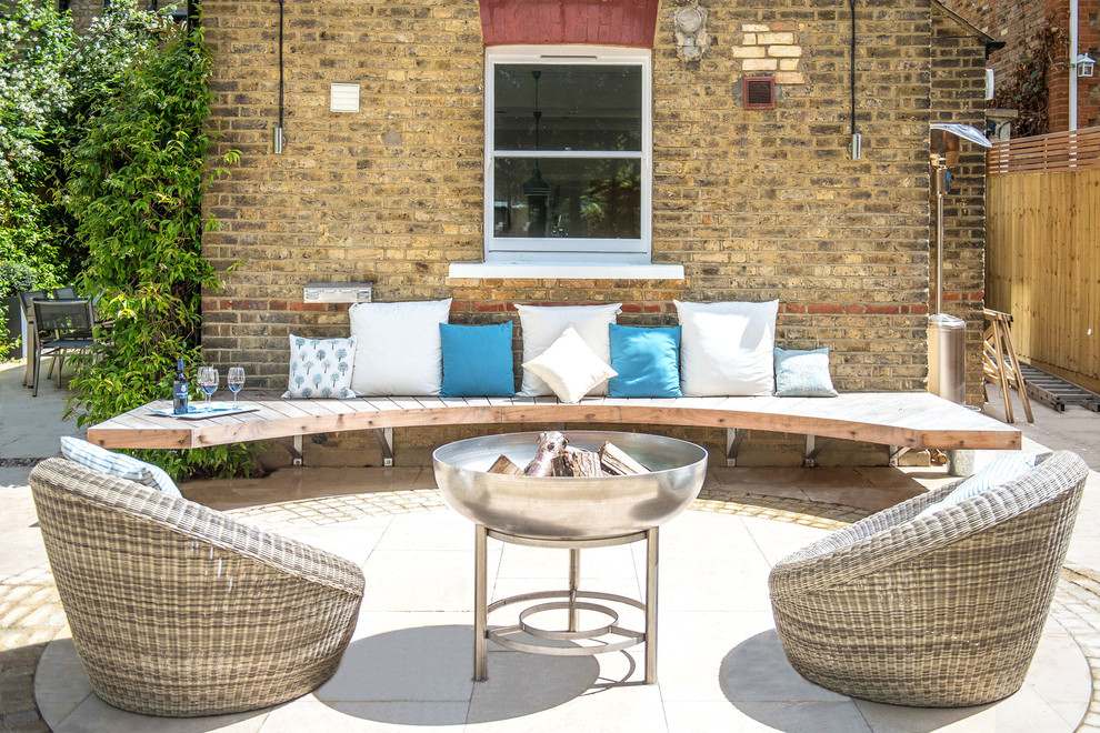 This is an example of a contemporary backyard patio in London with a fire feature and natural stone pavers.