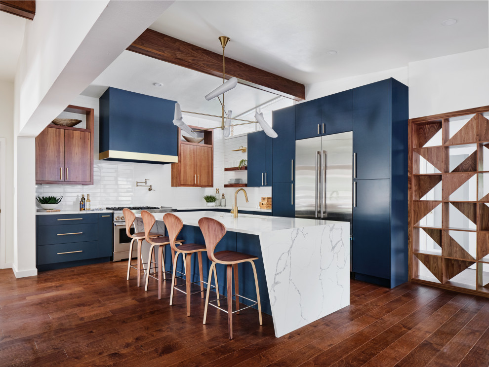 Photo of a large midcentury l-shaped open plan kitchen in Austin with a submerged sink, flat-panel cabinets, blue cabinets, engineered stone countertops, white splashback, ceramic splashback, stainless steel appliances, medium hardwood flooring, an island, brown floors, white worktops and exposed beams.