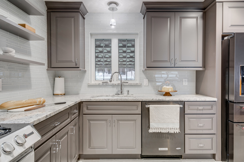 Inspiration for a mid-sized modern l-shaped kitchen pantry in Dallas with a drop-in sink, grey cabinets, granite benchtops, grey splashback, glass tile splashback, black appliances, porcelain floors, raised-panel cabinets, no island and grey benchtop.