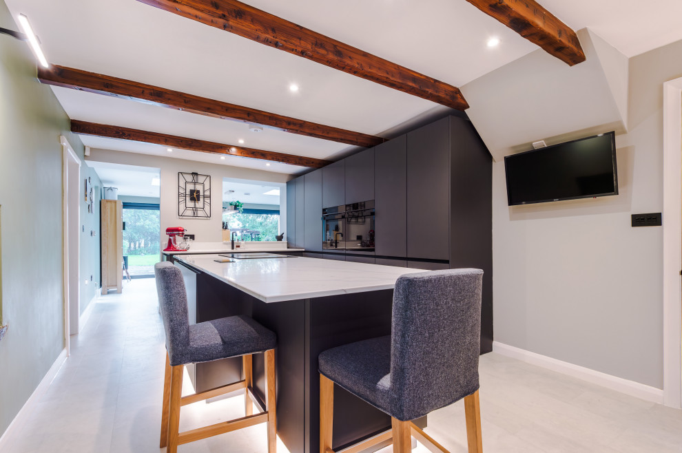 Photo of a medium sized contemporary galley open plan kitchen in Manchester with a built-in sink, flat-panel cabinets, grey cabinets, quartz worktops, glass sheet splashback, stainless steel appliances, an island, white worktops and a feature wall.