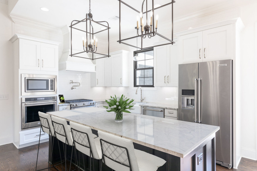 Example of a large transitional l-shaped dark wood floor and brown floor open concept kitchen design in Other with a farmhouse sink, recessed-panel cabinets, white cabinets, granite countertops, white backsplash, subway tile backsplash, stainless steel appliances, an island and gray countertops