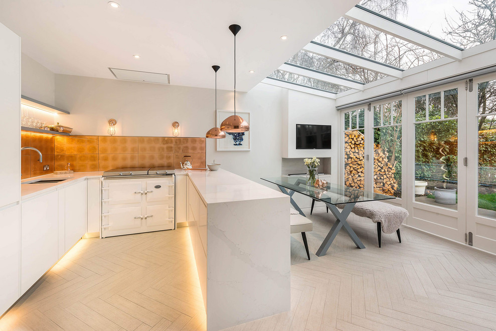 Photo of a contemporary u-shaped eat-in kitchen in London with a double-bowl sink, flat-panel cabinets, white cabinets, quartz benchtops, white appliances, porcelain floors, a peninsula, beige floor, white benchtop, metallic splashback and metal splashback.