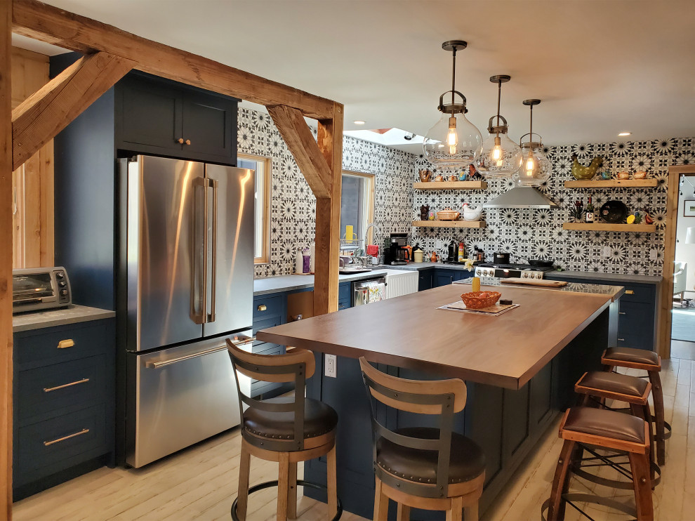 This is an example of a bohemian kitchen in New York with a belfast sink, beaded cabinets, blue cabinets, concrete worktops, stainless steel appliances, light hardwood flooring, an island, beige floors and brown worktops.