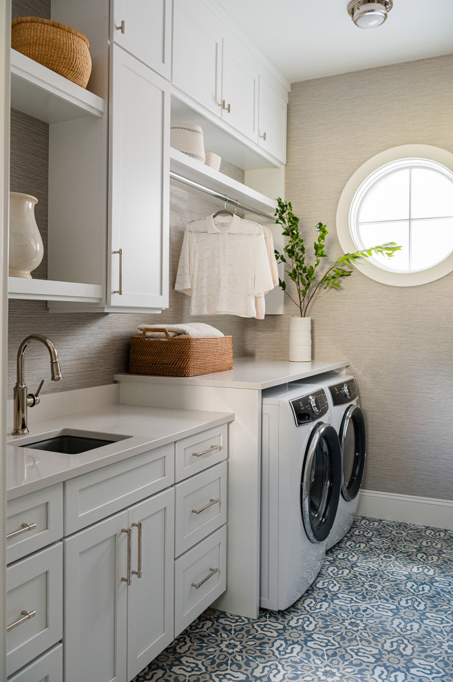 Example of a large beach style single-wall ceramic tile, multicolored floor and wallpaper dedicated laundry room design in Grand Rapids with an undermount sink, shaker cabinets, white cabinets, quartz countertops, beige walls, a side-by-side washer/dryer and white countertops