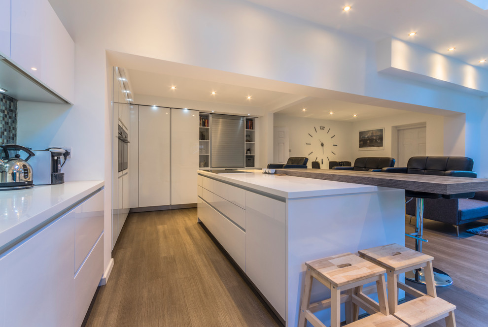 Design ideas for a modern kitchen/diner in Cheshire with flat-panel cabinets, white cabinets, medium hardwood flooring and an island.