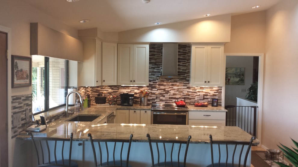 Open concept kitchen - mid-sized transitional u-shaped light wood floor open concept kitchen idea in Phoenix with a single-bowl sink, flat-panel cabinets, white cabinets, granite countertops, brown backsplash, glass tile backsplash, stainless steel appliances and a peninsula