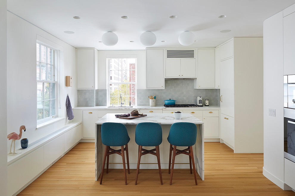 Photo of a mid-sized contemporary l-shaped eat-in kitchen in New York with an undermount sink, flat-panel cabinets, white cabinets, grey splashback, with island, marble benchtops, ceramic splashback, panelled appliances and light hardwood floors.