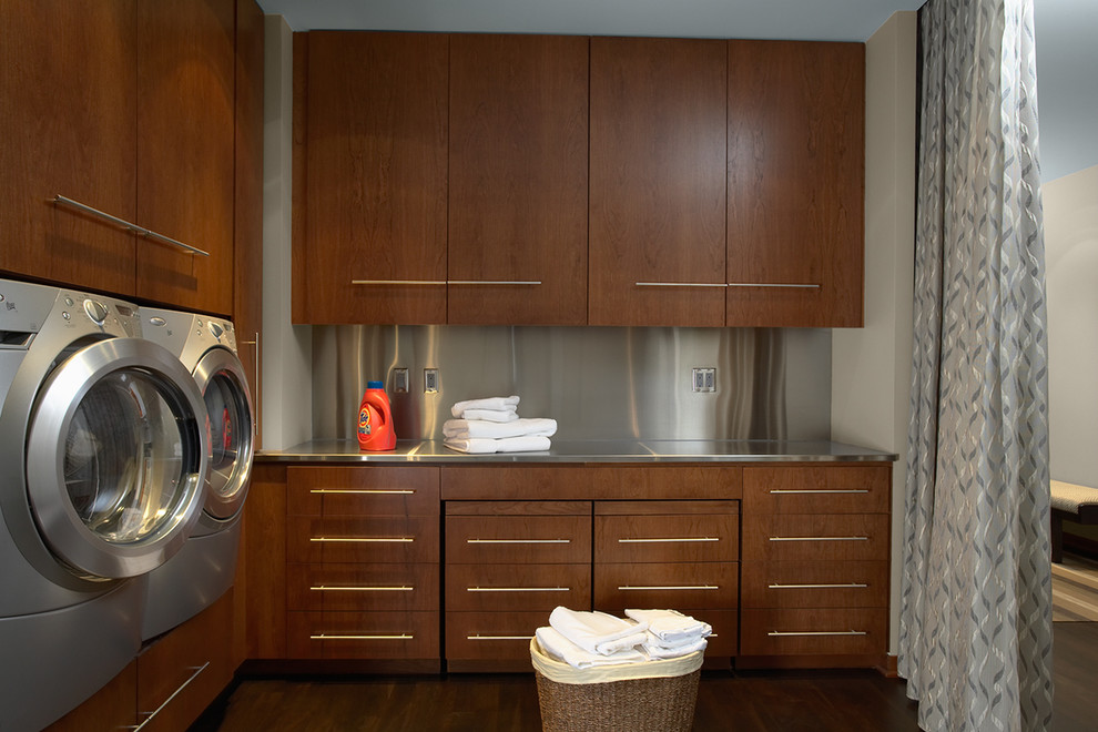 Design ideas for a contemporary l-shaped laundry room in Minneapolis with flat-panel cabinets, medium wood cabinets, stainless steel benchtops, beige walls, dark hardwood floors and a side-by-side washer and dryer.