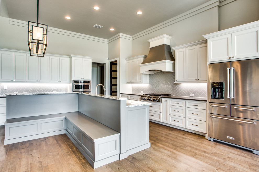 Open concept kitchen - transitional l-shaped medium tone wood floor and brown floor open concept kitchen idea in Austin with recessed-panel cabinets, white cabinets, gray backsplash, ceramic backsplash, stainless steel appliances, an island and gray countertops