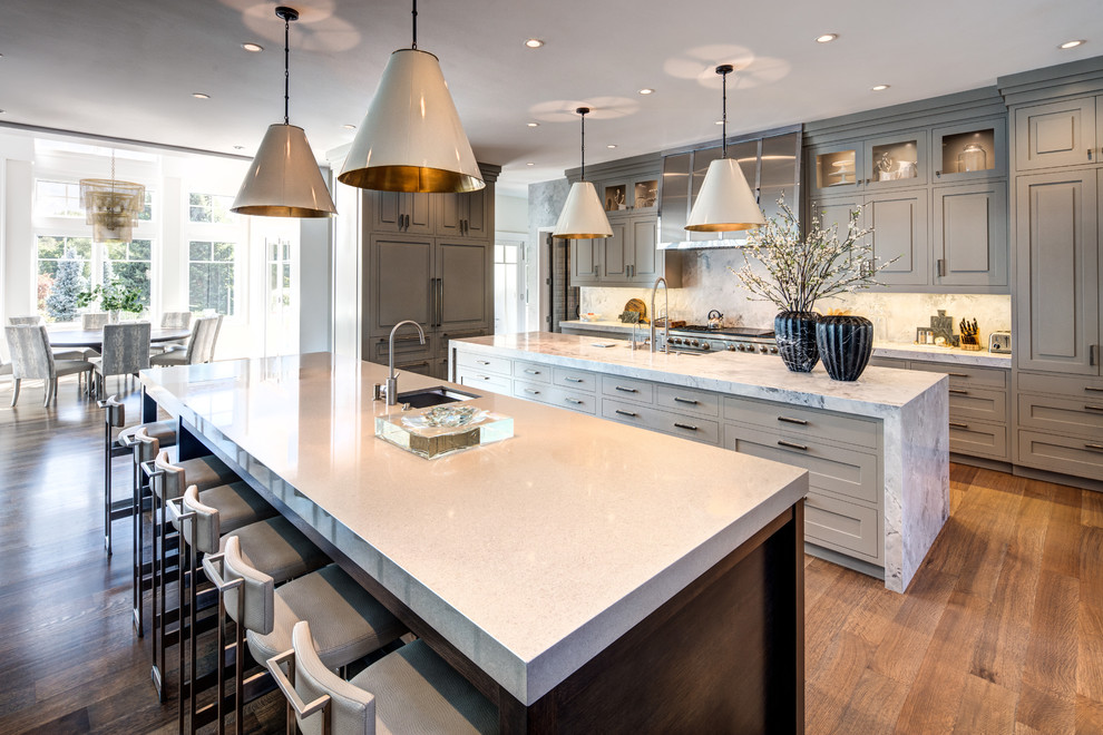 Design ideas for an expansive transitional l-shaped eat-in kitchen in Salt Lake City with grey cabinets, multiple islands, an undermount sink, shaker cabinets, white splashback, stone slab splashback, panelled appliances, medium hardwood floors, brown floor and white benchtop.