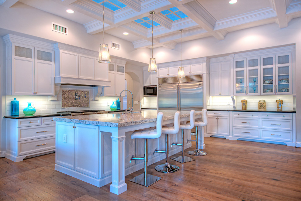 Design ideas for a large transitional l-shaped eat-in kitchen in Phoenix with a farmhouse sink, recessed-panel cabinets, white cabinets, granite benchtops, white splashback, subway tile splashback, stainless steel appliances, medium hardwood floors and with island.