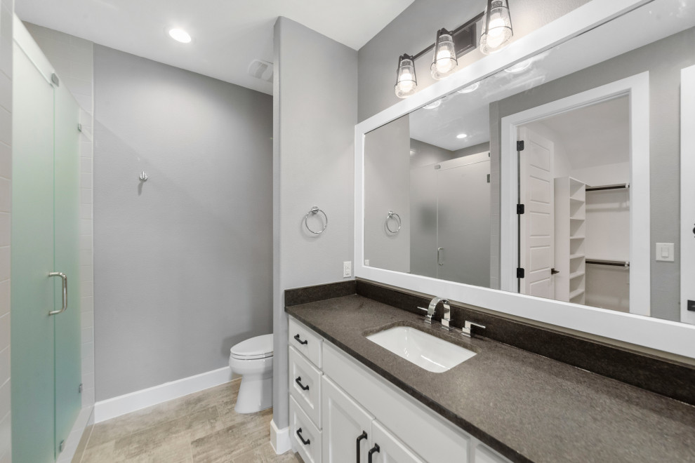 Design ideas for a mid-sized contemporary 3/4 bathroom in Dallas with recessed-panel cabinets, white cabinets, a corner shower, a one-piece toilet, grey walls, ceramic floors, an undermount sink, granite benchtops, grey floor, a hinged shower door, black benchtops, a single vanity and a built-in vanity.