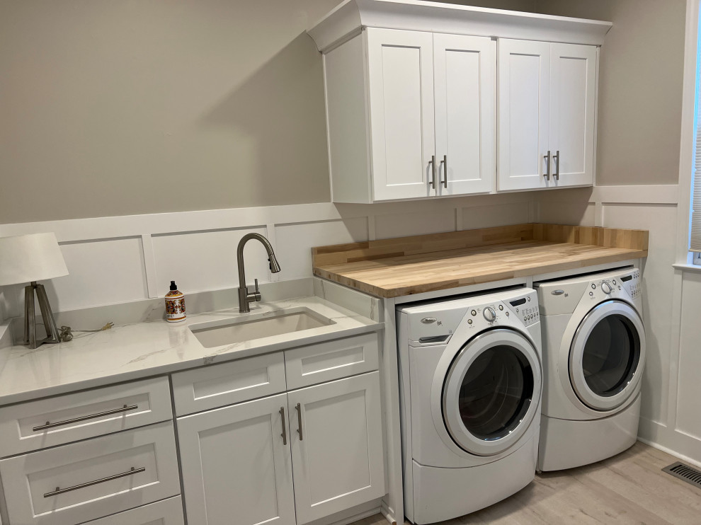 Large transitional single-wall utility room in Atlanta with a single-bowl sink, shaker cabinets, white cabinets, wood benchtops, white splashback, timber splashback, grey walls, vinyl floors, a side-by-side washer and dryer, grey floor, brown benchtop and wood walls.